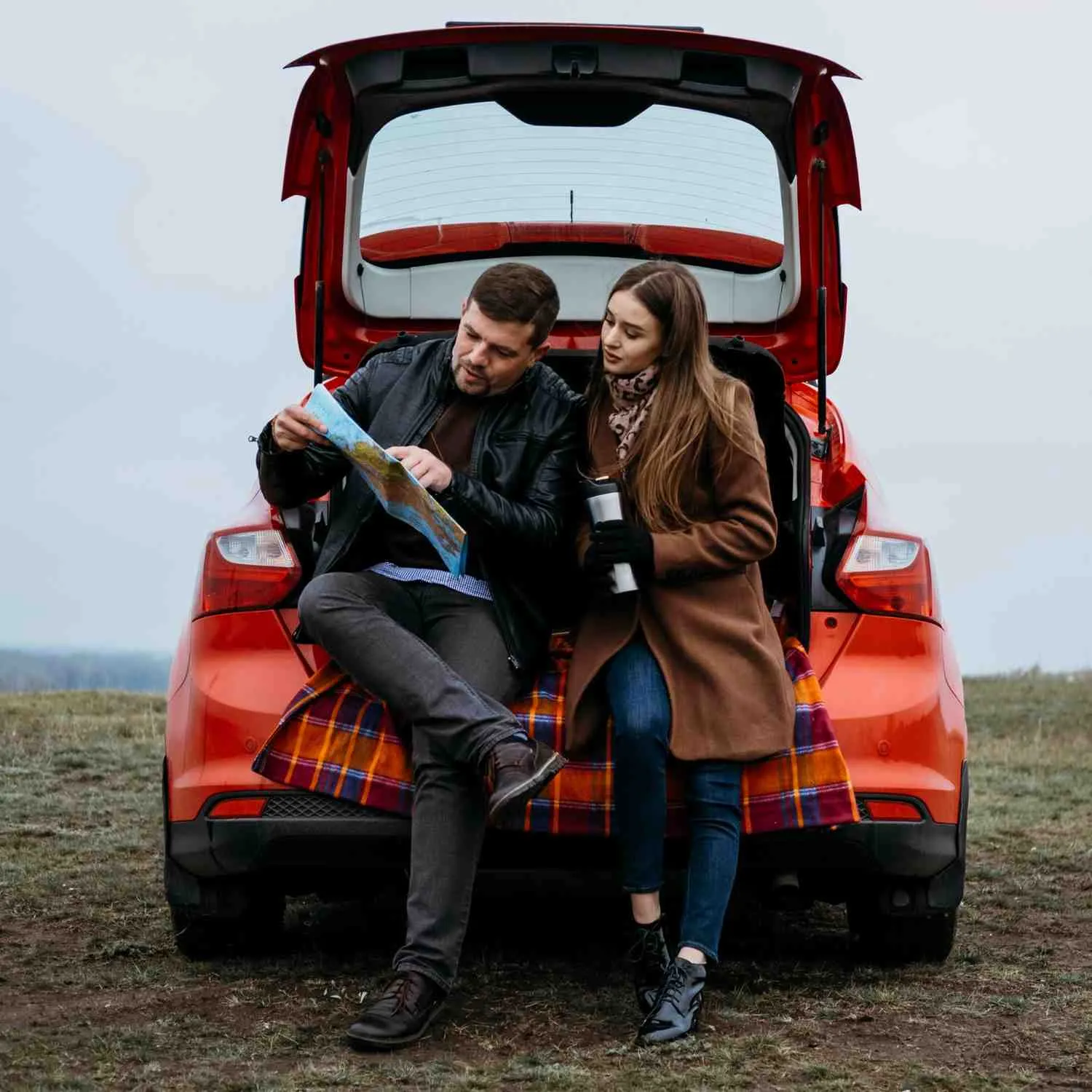 Two drivers sitting at the open trunk of their car with a road map